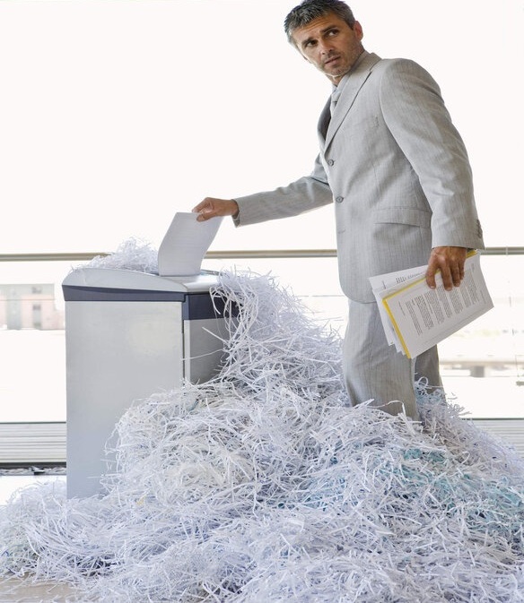 کارمندی در حال خرد کردن اسناد شرکت با دستگاه های اداری کاغذ خرد کن که حجم زیادی کاغذ تولید کرده است