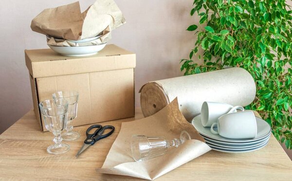 بسته بندی تعدادی ظرف و لیوان با کاغذ و روزنامه روی یک میز چوبی
